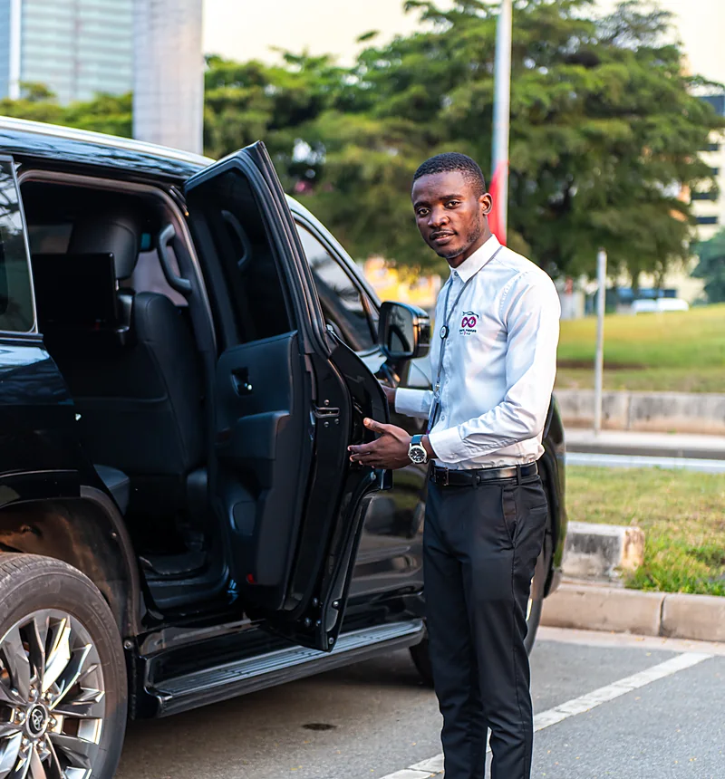Uniformed Costa Phoebe driver holding open the door of a black Land Cruiser